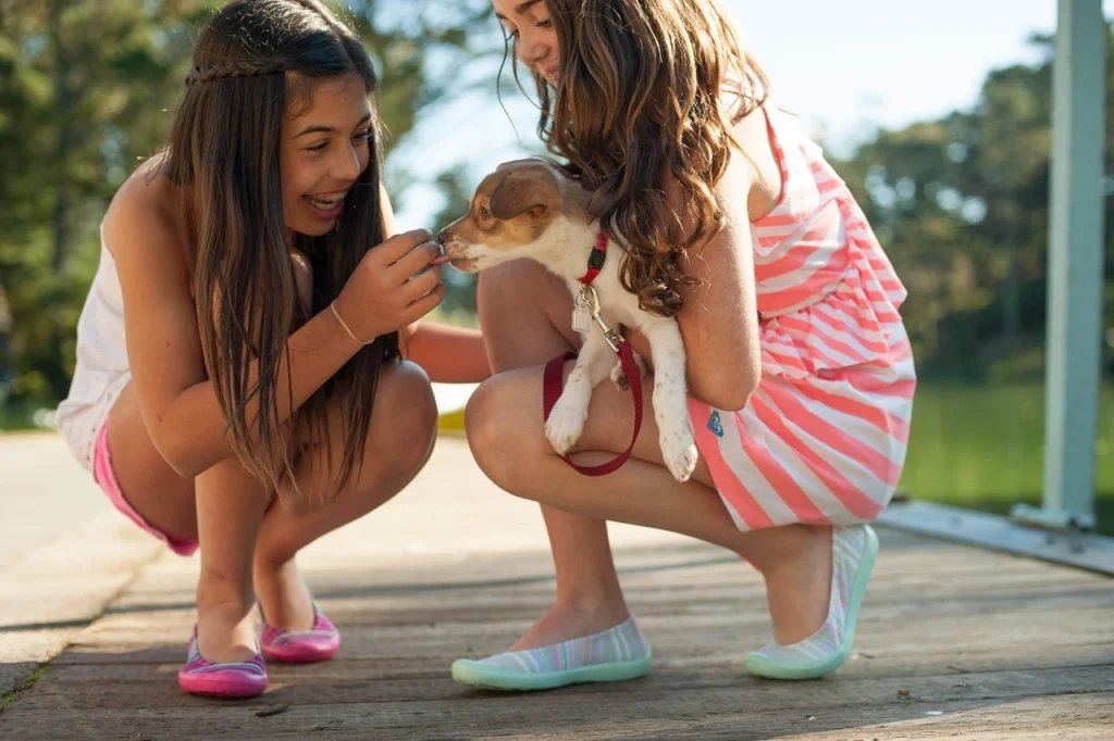 duas meninas brincando com filhote de cachorro ilustrando o assunto das melhores raças de cachorro para crianças
